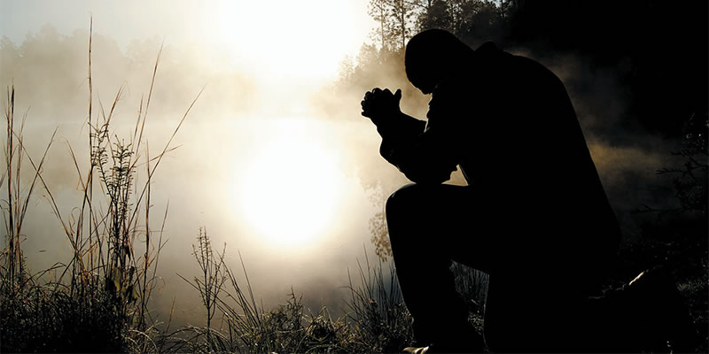 Man kneeling in prayer in the early dawn.