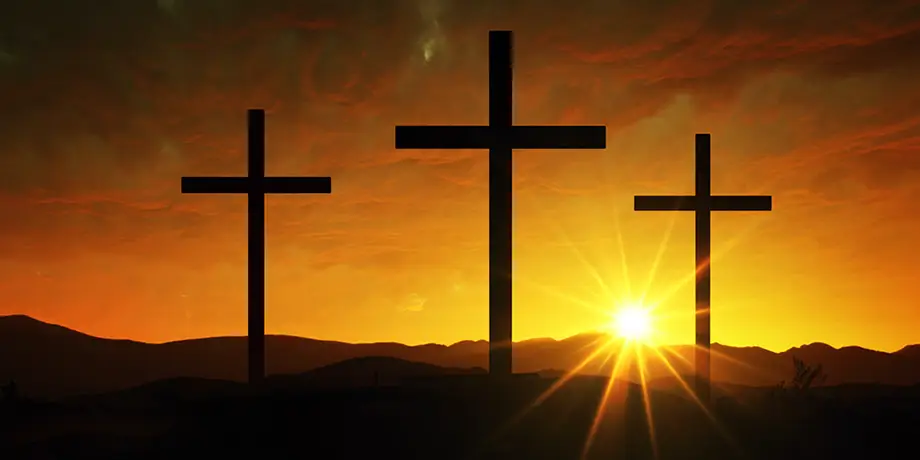 Three crosses on a hill with the setting sun behind them.