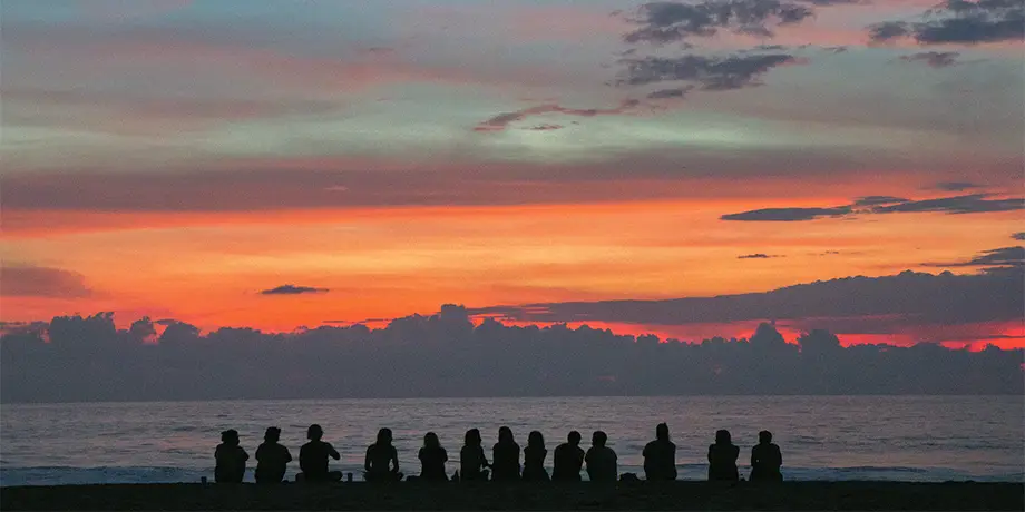 Youth sitting in a line facing the sea looking at the sunset