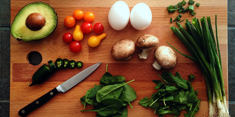 Avacado, onions, tomatos, eggs, mushrooms and leafy greens on a cutting board