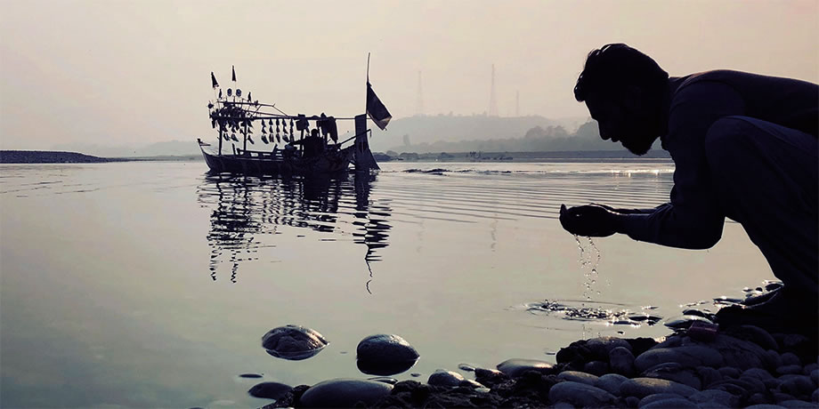 A man kneeling by a lake hands cupped with lake water.