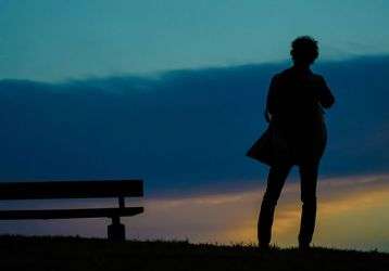 Solitary person standing on a hillside near a park bench