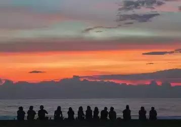 Youth sitting in a line facing the sea looking at the sunset